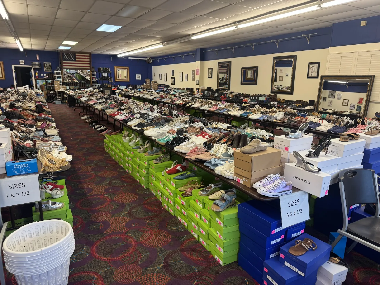Inside The Shoe Room: long tables packed with shoes sorted by size, designer boxes stacked alongside, and a basket ready by the aisle.